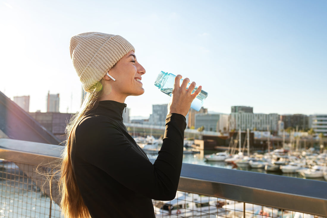 Woman in long sleeves and winter hat smiling and drinking water 